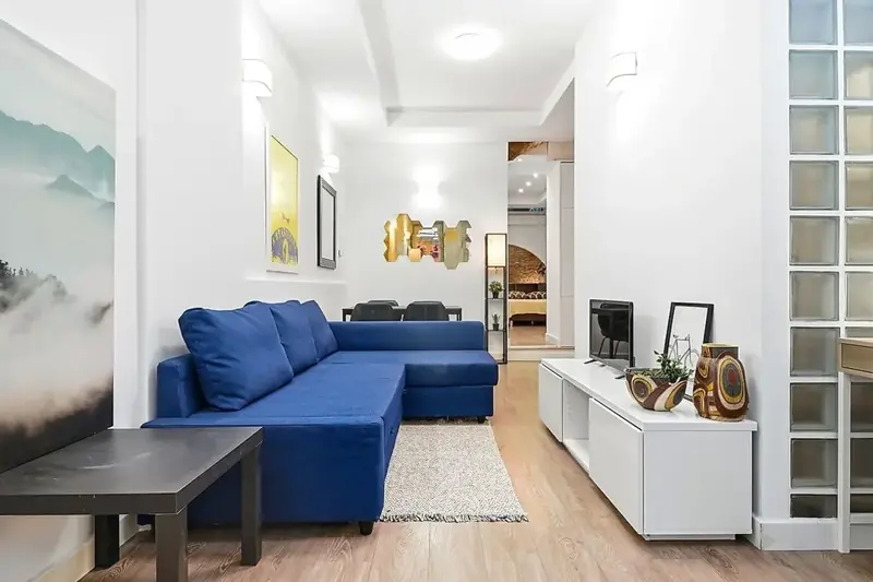 Sala de um apartamento em Lisboa acabado de pintar, com paredes e tetos brancos e sofá azul