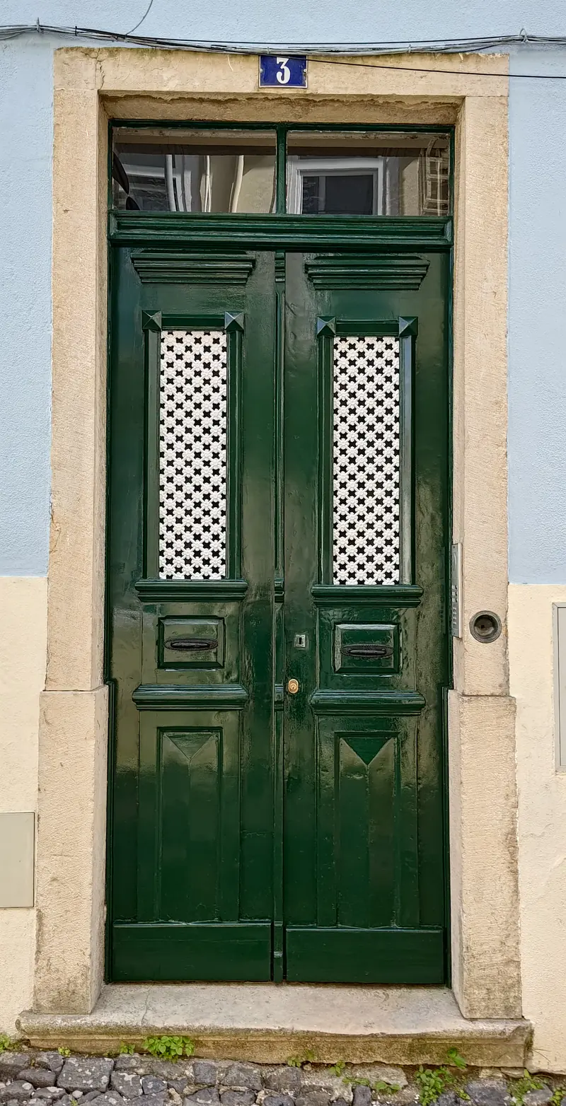 Porta de entrada restaurada em verde-escuro, numa fachada azul-clara de Lisboa