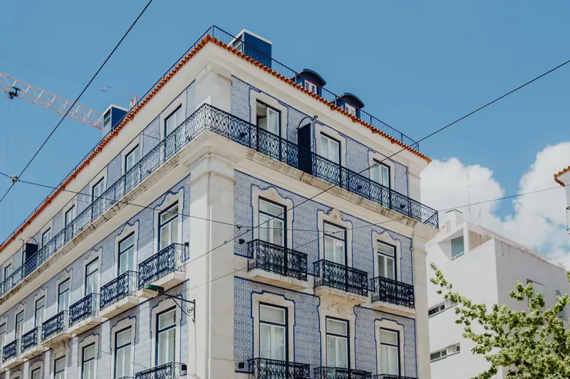 Prédio de esquina em Lisboa, revestido a azulejo azul e branco, com varandas de ferro