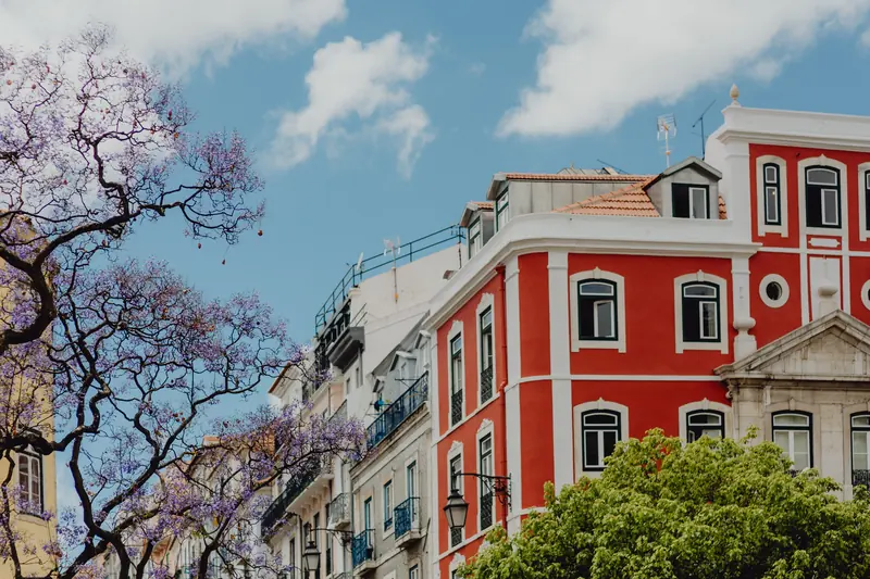 Prédio vermelho com cantarias brancas em Lisboa, sob um céu azul
