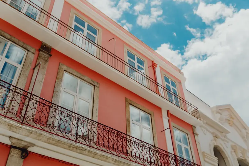 Fachada cor de salmão com varanda de ferro e céu com nuvens