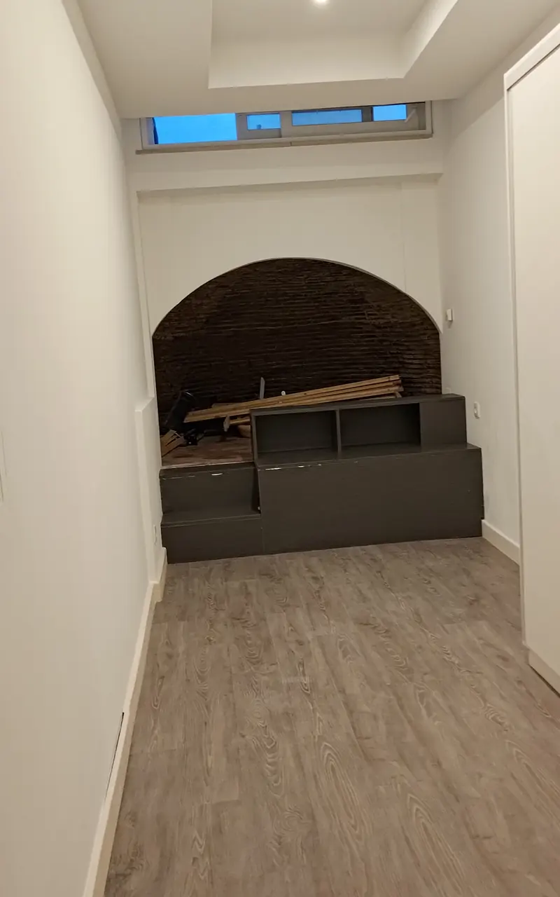 Quarto estreito em cave com paredes brancas acabadas de pintar e arco de tijolo ao fundo