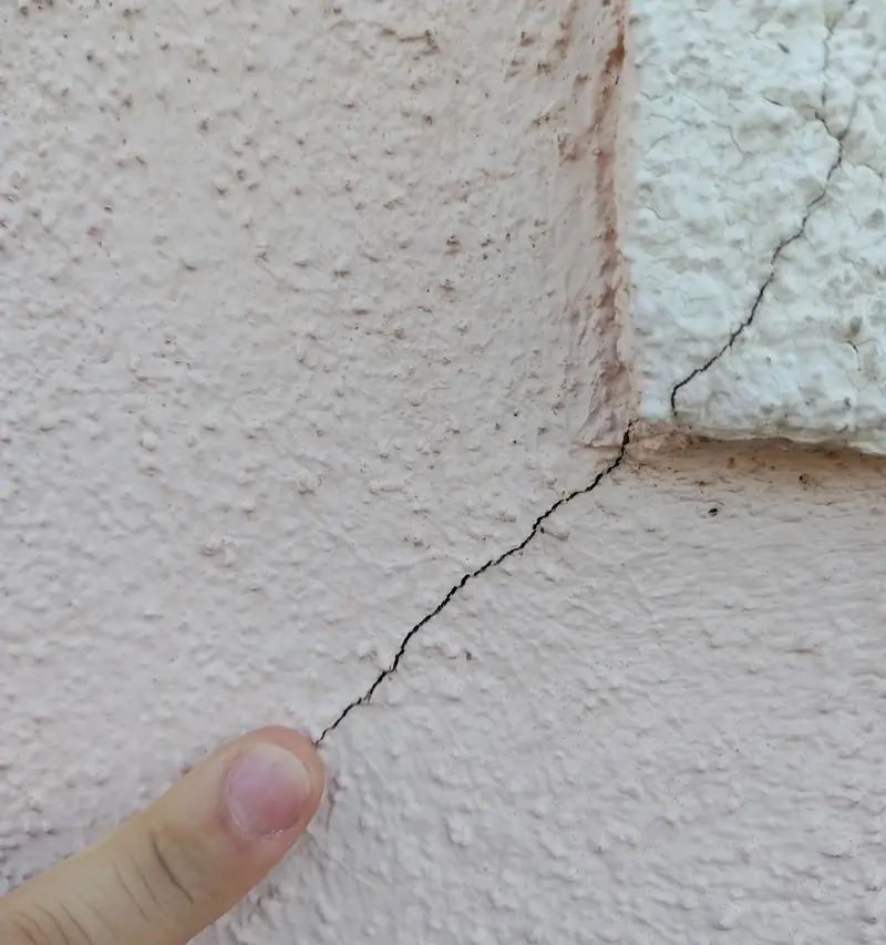 Dedo a apontar uma fissura fina num reboco exterior cor-de-rosa