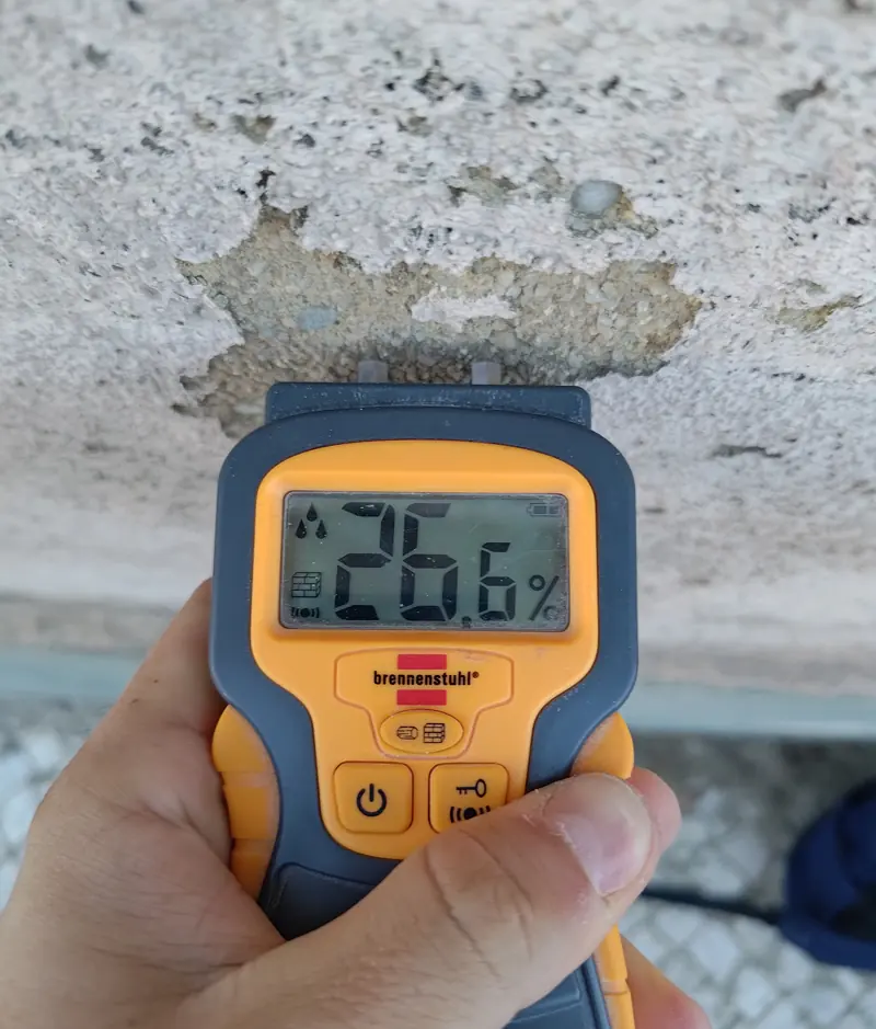 Medidor de humidade a marcar 26,6% numa parede exterior com reboco degradado