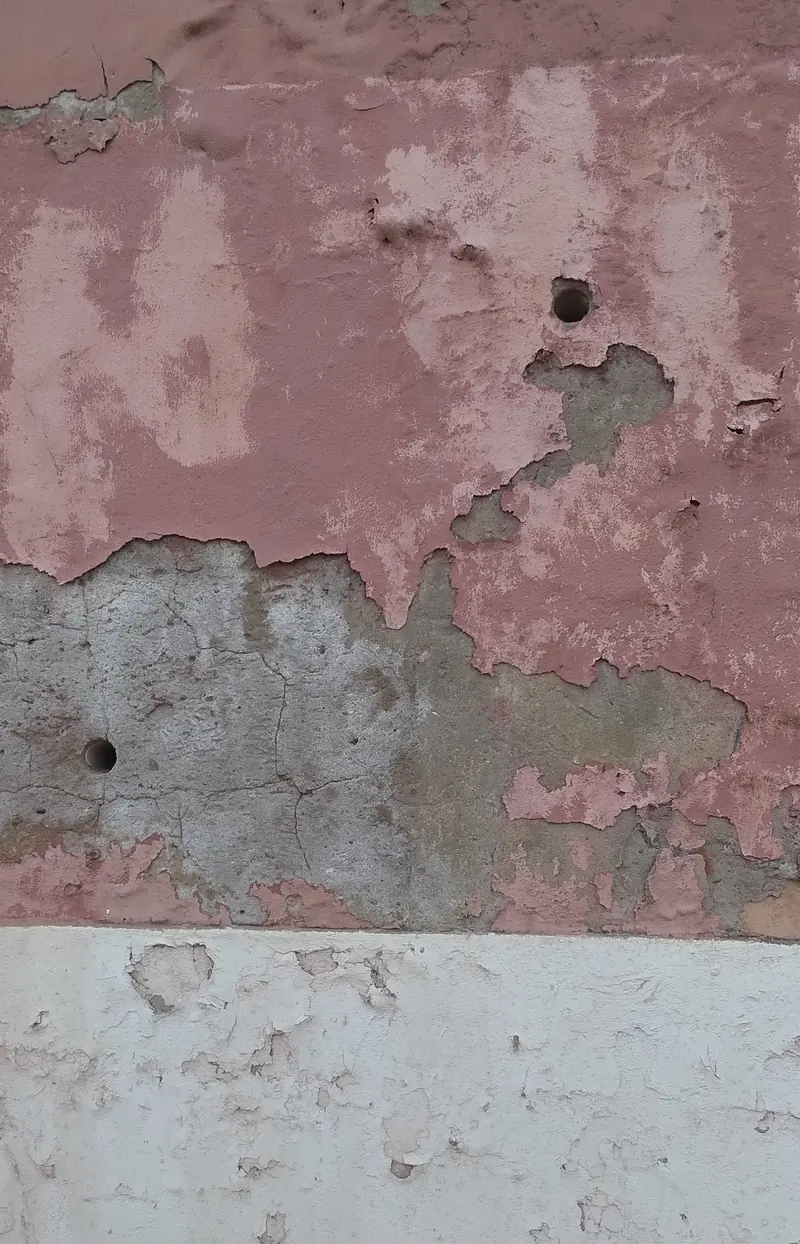 Tinta cor-de-rosa a soltar-se em placas de uma fachada, com o reboco à vista